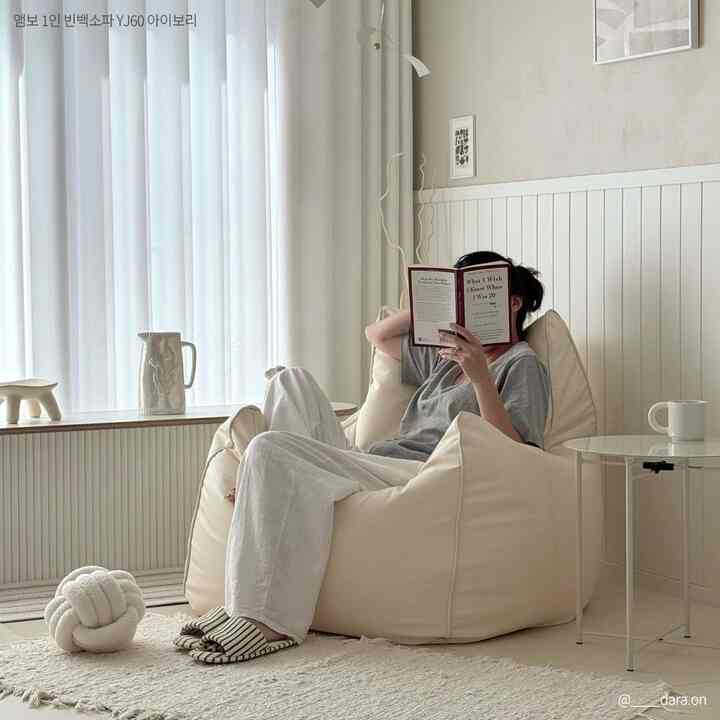 Ivory-toned living room featuring a comfortable bean bag sofa centrally placed with side table and person reading, creating a cozy atmosphere