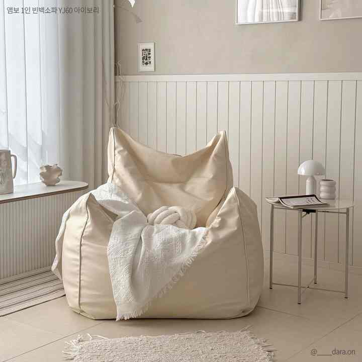 アイボリー調のワンルームリビング、大きなビーズクッションソファと白いラグが配置された居心地の良いインテリア