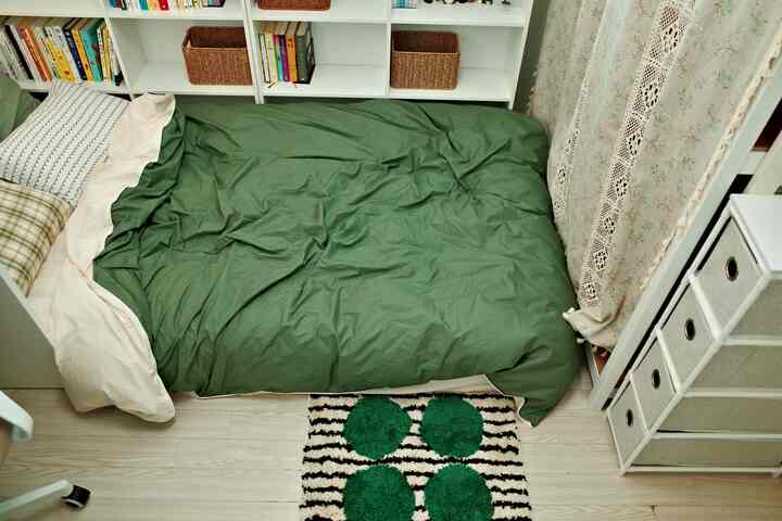 白と緑のトーンが中心の寝室、緑の掛け布団カバーのベッドと壁際に配置された本棚がある雰囲気のある空間