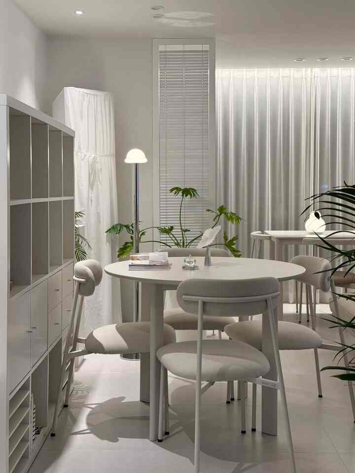 White-toned dining room featuring a round dining table, chairs, floor lamp, and blinds creating a modern and clean ambiance