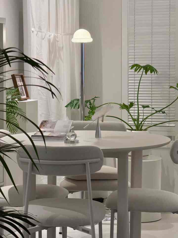 ホワイトトーンのリビング、丸いダイニングテーブルとフロアランプ、植物が配置されたミニマルで雰囲気のあるインテリア