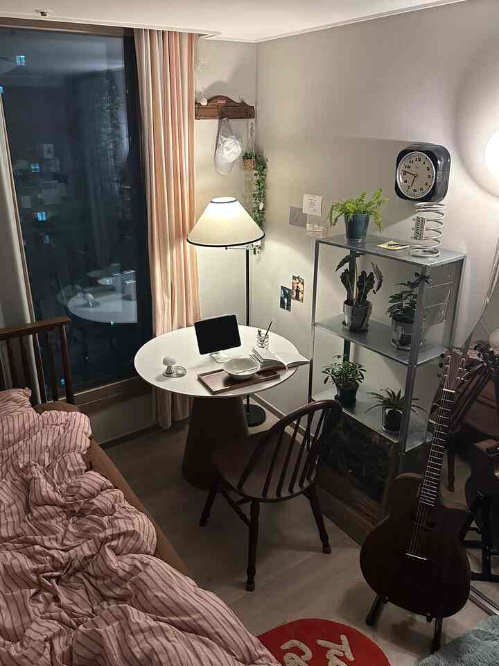 ナチュラルトーンの2.5坪寝室、木製の丸テーブルと植物の棚、ヴィンテージ家具が調和した温かみのある空間