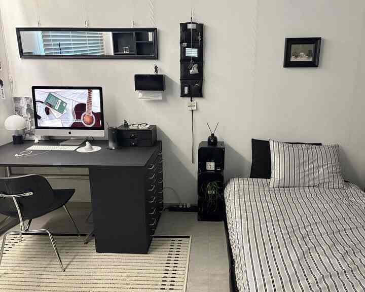 A modern bedroom and home office space in black and ivory tones, featuring a black desk and striped rug dividing the area