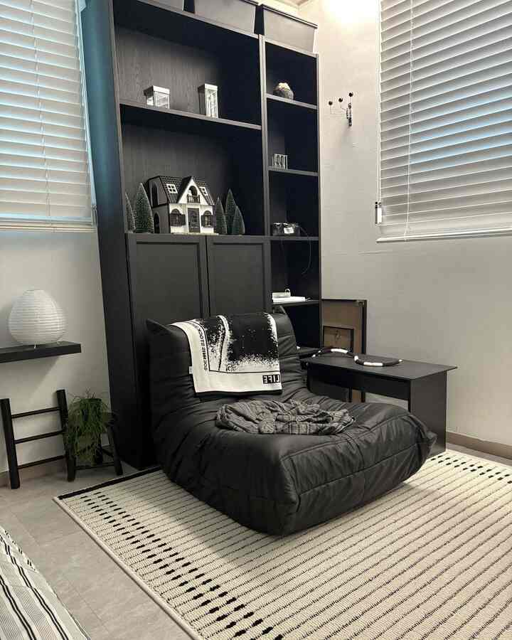 Monotone living room featuring black sofa and bookshelf with striped ivory rug, showcasing a simple and modern aesthetic