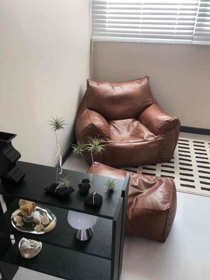 Minimal living room with brown bean bag sofa and black shelf, featuring simple decor and natural tones