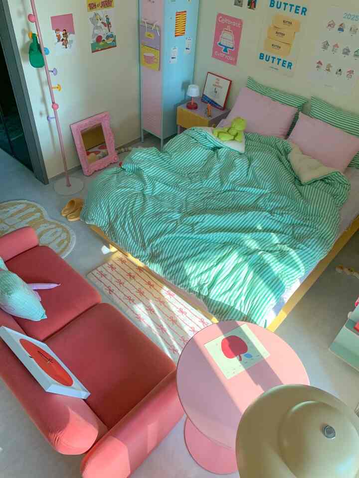 パステルピンクとグリーンのストライプ寝具が特徴の可愛らしい子供部屋、ピンクのソファとカラフルな壁ポスターが配置された雰囲気のあるインテリア