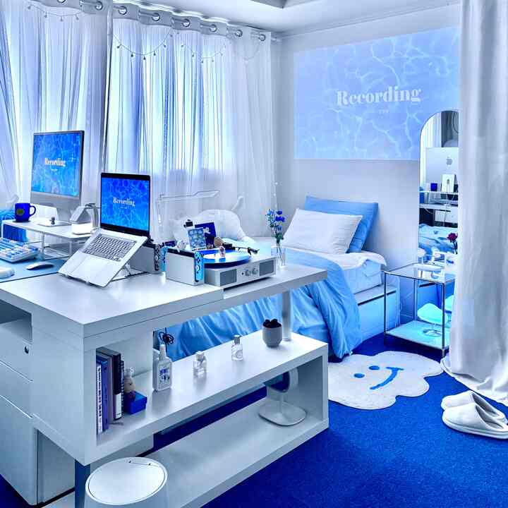 涼しげなブルーとホワイトのトーンのワンルーム寝室、デュアルモニターのデスクと整ったインテリアが調和した雰囲気のある空間