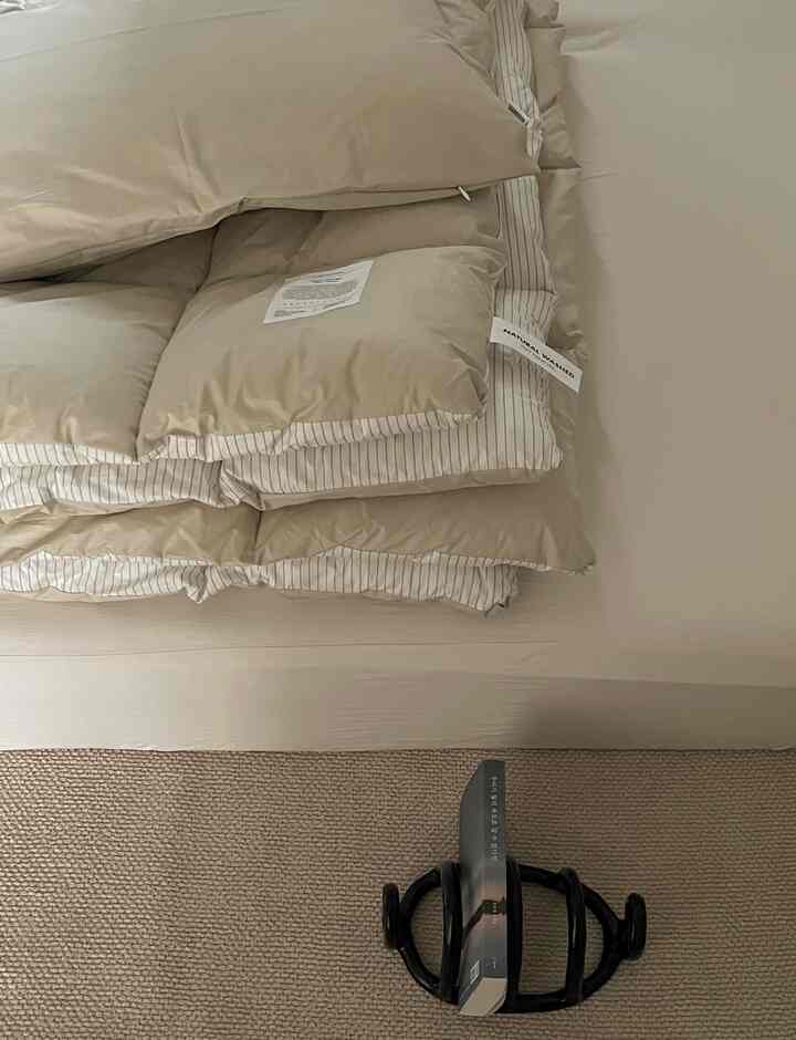 温かみのあるベージュ調の寝室、きれいに畳まれた掛け布団カバーとベージュのラグが配置された雰囲気のある空間