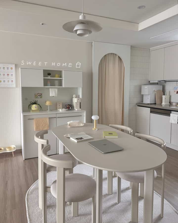 白とベージュのトーンが調和したナチュラルで清潔感のあるキッチン空間、アーチ型の間仕切りとダイニングテーブル、照明が配置されたおうちカフェスタイルのインテリア