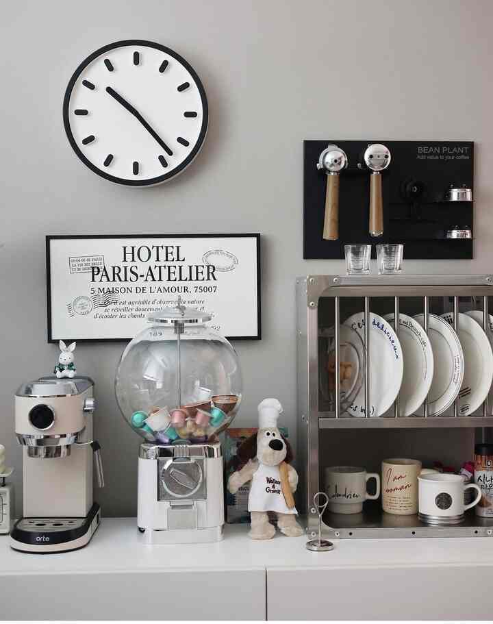 A neat home cafe setup with gray walls, white appliances, a coffee capsule dispenser, wall clock, and a poster