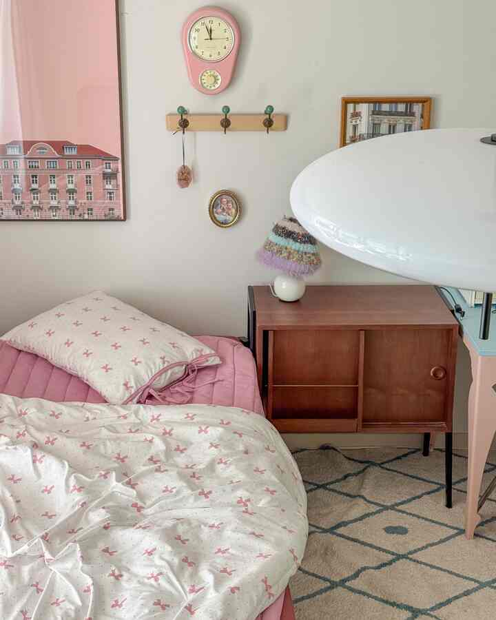 ピンクと白の色調の子供部屋、リボン柄の寝具と木目調のナイトスタンドが配置されたかわいい寝室のインテリア