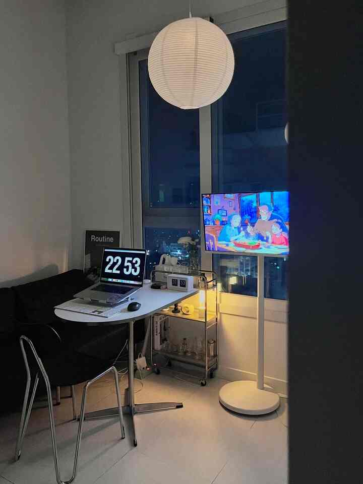 明るくモダンな白いワンルームリビング、ペンダントライトとフロアランプ、コンピューターとテレビが配置された居心地の良い空間