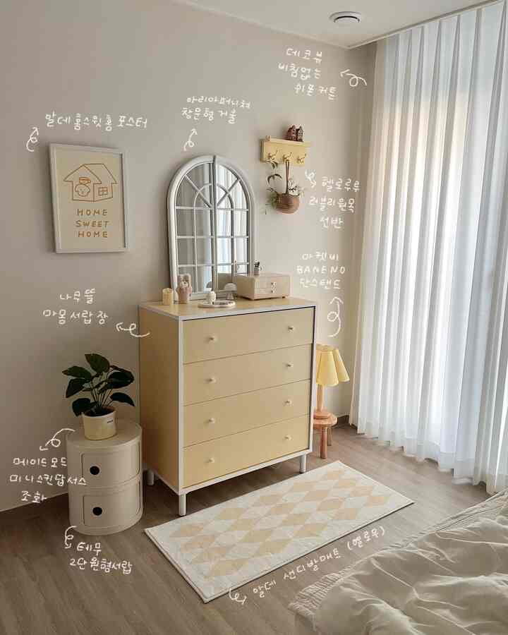 アイボリーの壁と黄色のチェストが配置された寝室、木製の床と白いシフォンカーテンが暖かくナチュラルな雰囲気のあるインテリア