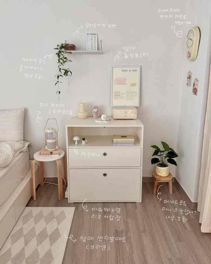 白と茶色のトーンの寝室、ベッド横にチェストと照明、ポスター、植物が配置された雰囲気のあるインテリア