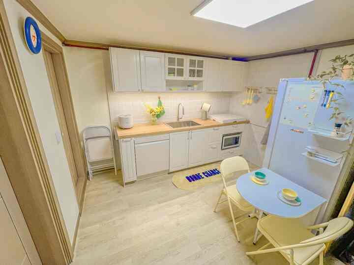 明るい白と木目調が調和したコンパクトなキッチンスペース、折りたたみ椅子とテーブルが配置された実用的な新婚家のインテリア