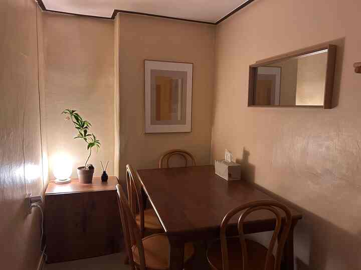 A compact dining room in natural brown tones featuring a wooden dining table with four chairs, picture frame, and mirror creating a simple and cozy atmosphere