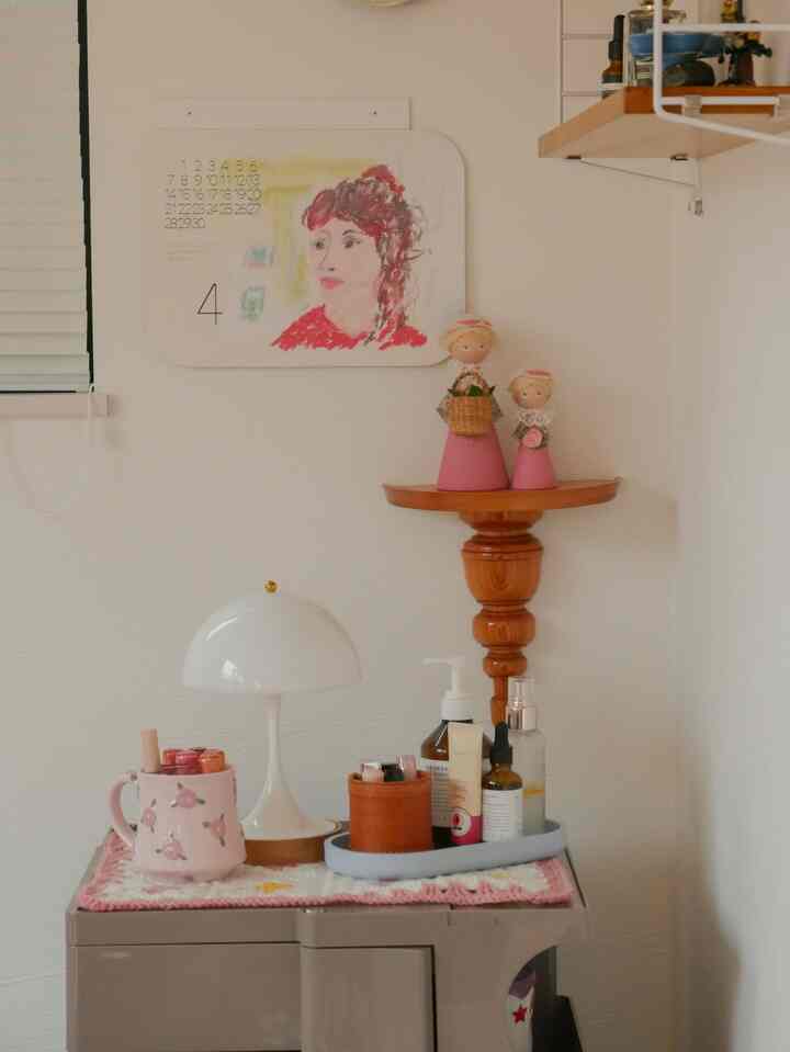 ホワイトの壁とピンクの小物が調和する北欧ヴィンテージのパウダールーム、小型家具が配置された印象的な空間