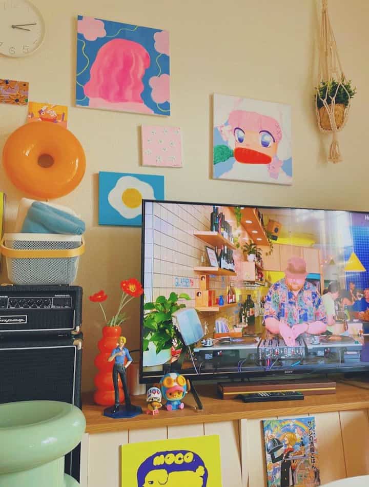 Bright orange, blue, and pink toned living room featuring iconic wall art, IKEA furniture, and charming decorative objets