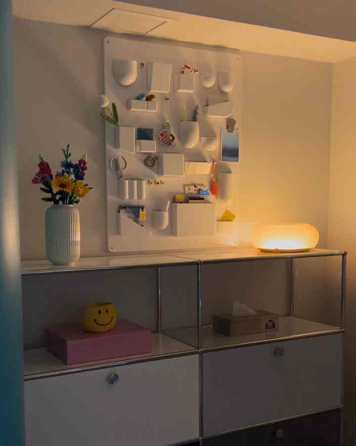 暖かい照明と共に壁掛け収納と花瓶が配置された白い壁のモダンな収納空間