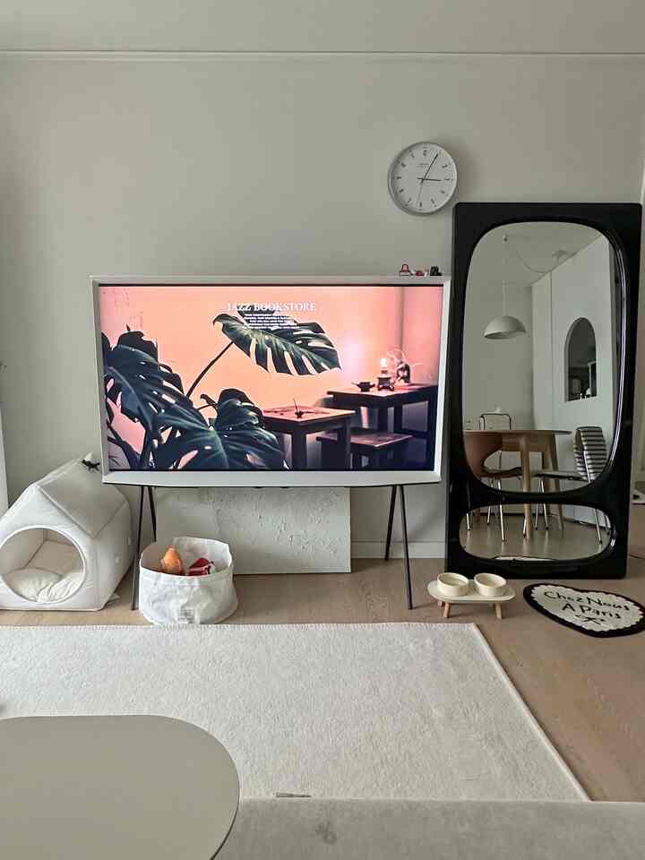 ホワイトとベージュ調のリビング、セリフTVや全身鏡、ペットハウスと犬用食器が配置されたすっきりとした空間