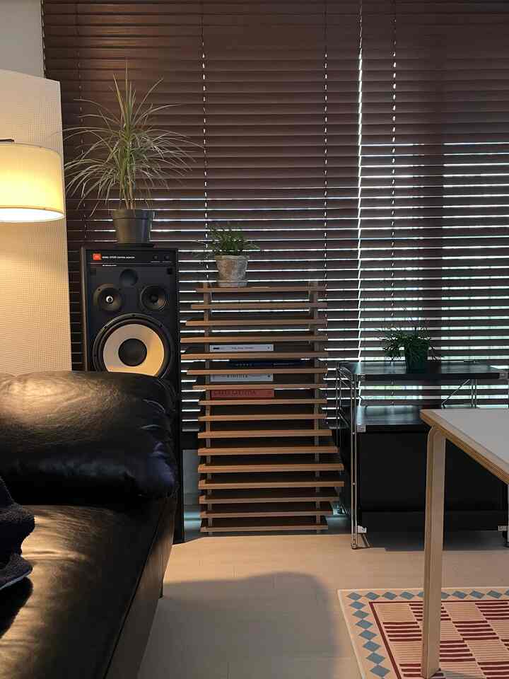 Wood tone and black themed living room with wooden slatted shelf, blinds, black leather sofa, and floor lamp creating a cozy atmosphere