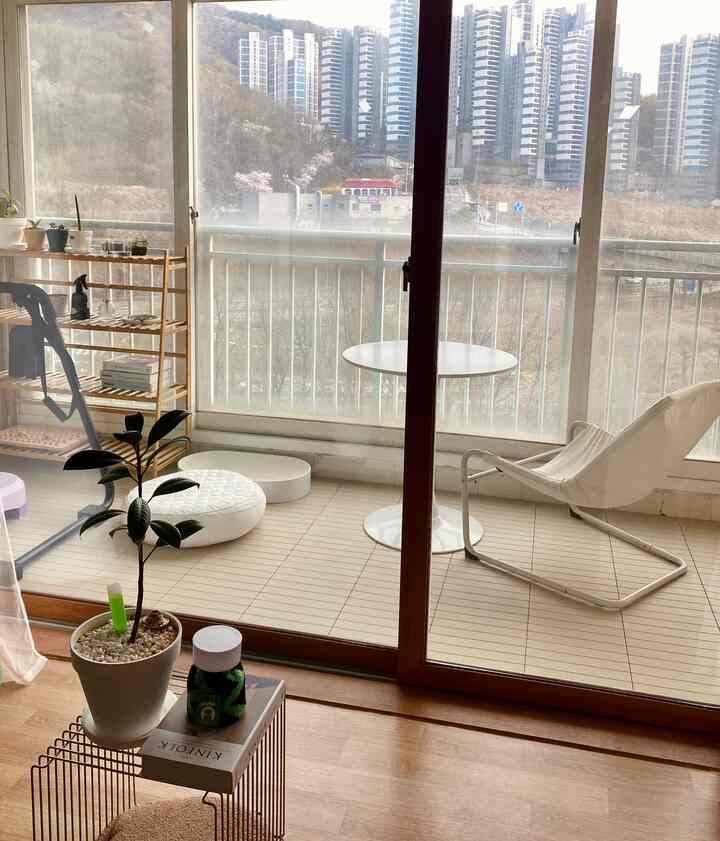 ナチュラルな木目調とホワイトの調和が美しいベランダ、円形テーブルとアームチェアが配置された落ち着いた雰囲気のインテリア