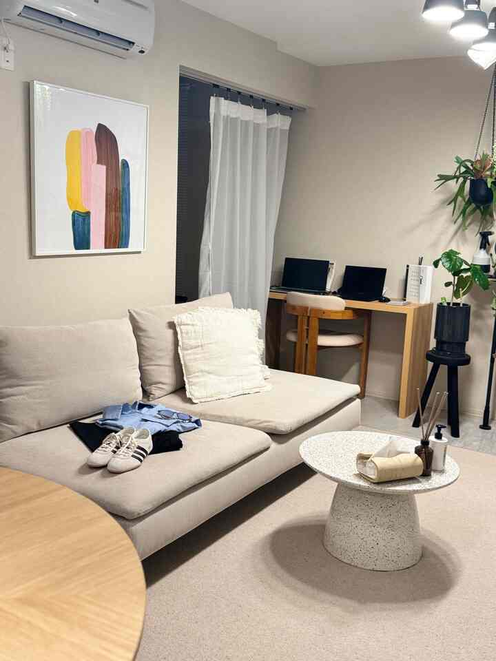 ベージュとグレーのトーンのリビング、ソファとコーヒーテーブル、デスクと植物が配置された落ち着いた自然な雰囲気の空間