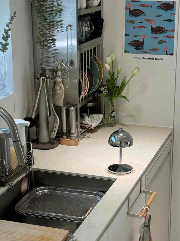 白とクロムの調和がとれたキッチン、調理器具とクロムのテーブルランプが配置されたモダンな空間