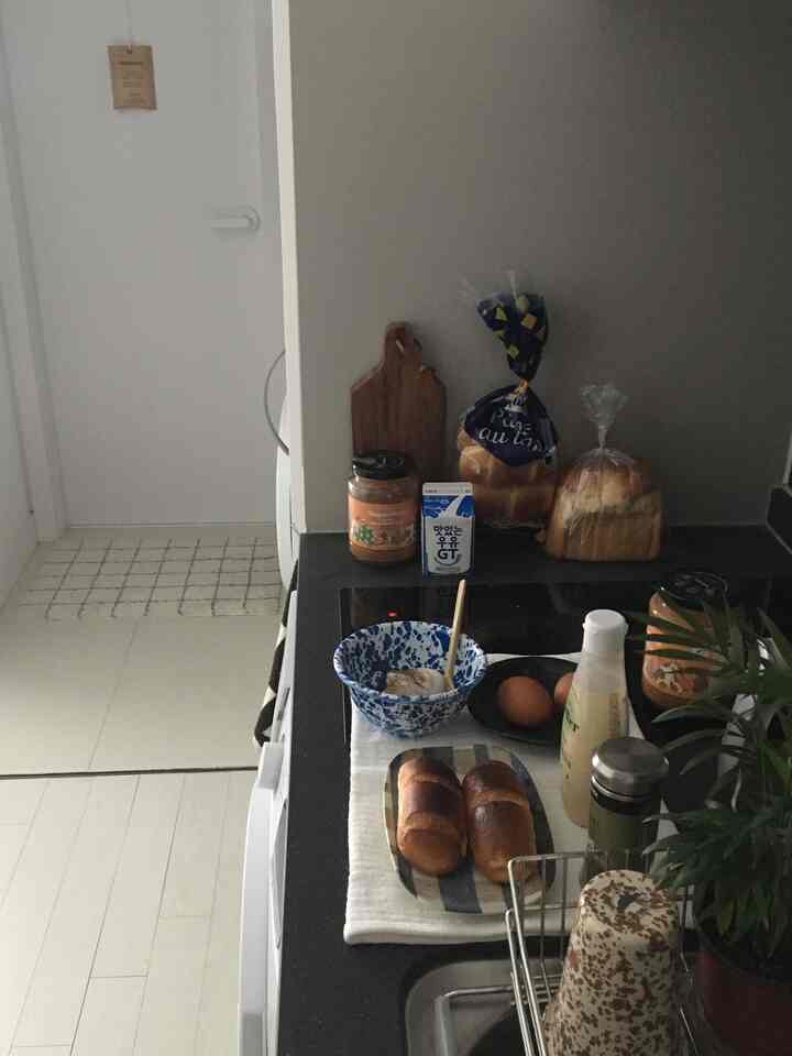 白とグレー調のワンルームキッチン、清潔なカウンターにパンと皿が置かれた雰囲気のあるインテリア