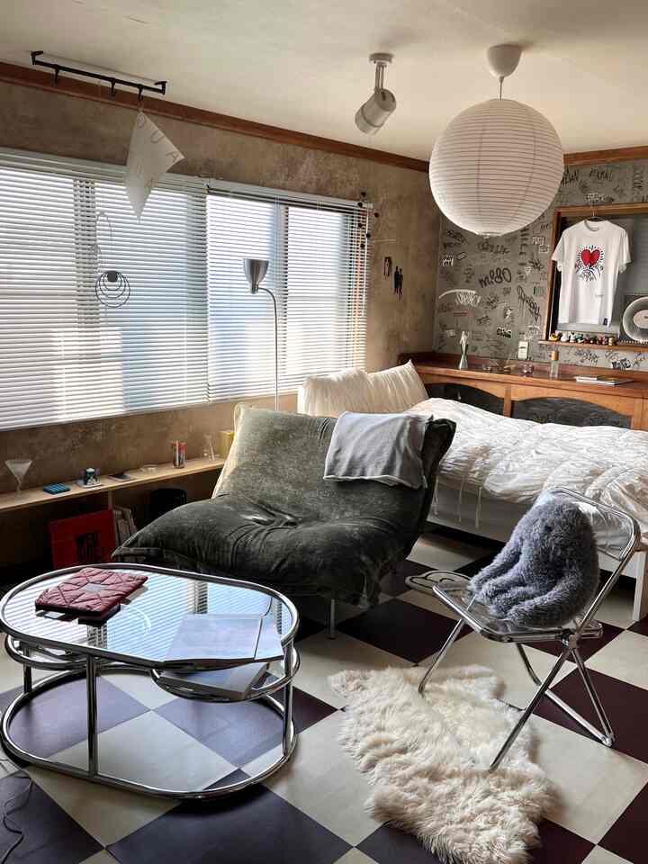 A vintage-style living room featuring white bedding, green sofa, checkered floor, and white blinds with a cozy atmosphere