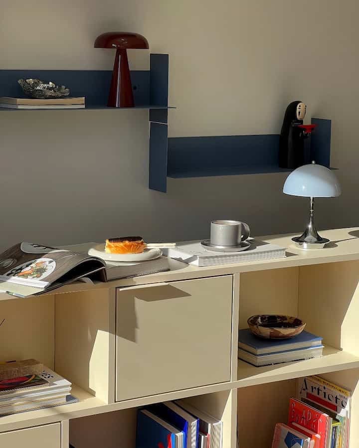 Natural-toned dining room with blue shelves, featuring table lamps, coffee, and cake creating a cozy home cafe atmosphere