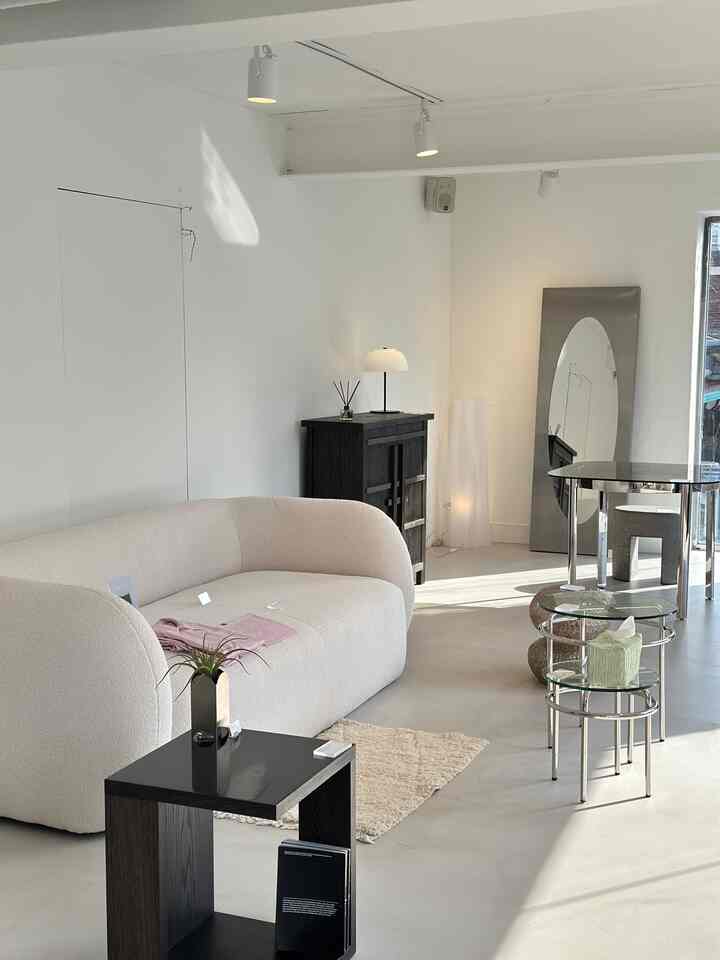 Modern showroom living room in white and light gray tones, featuring a curved sofa, black furniture, and stylish interior accessories