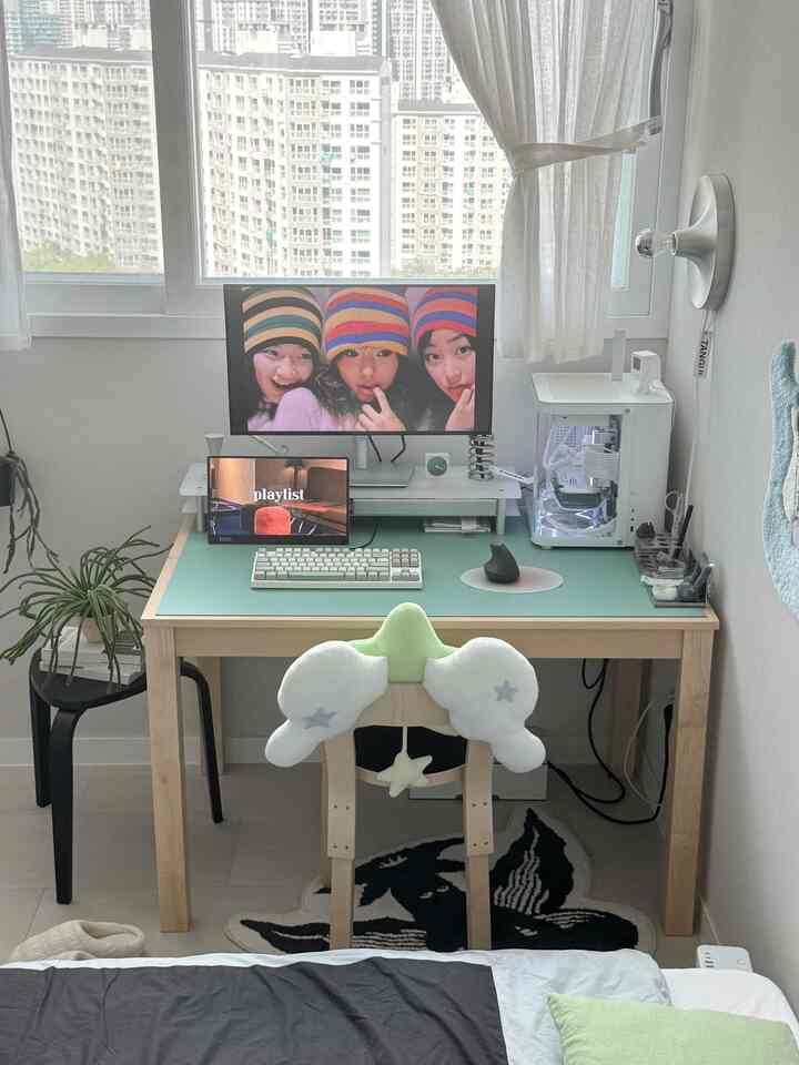 白とウッドトーン、グリーンの寝室とホームオフィス空間、モニターとデスク、椅子が整然と配置された快適な作業環境