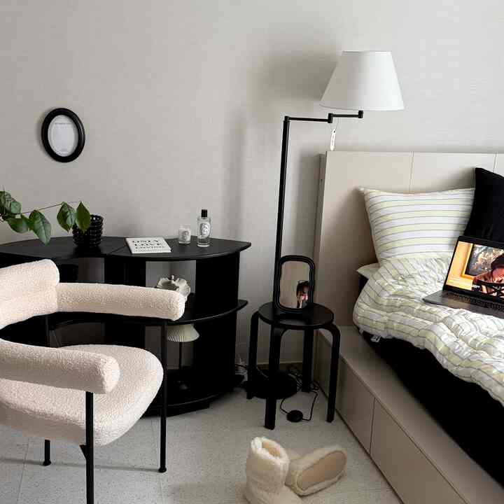 ホワイトとブラックのナチュラルモダン寝室、クリーム色のアームチェアとミッドセンチュリースタイルの黒い棚が配置された落ち着いた空間