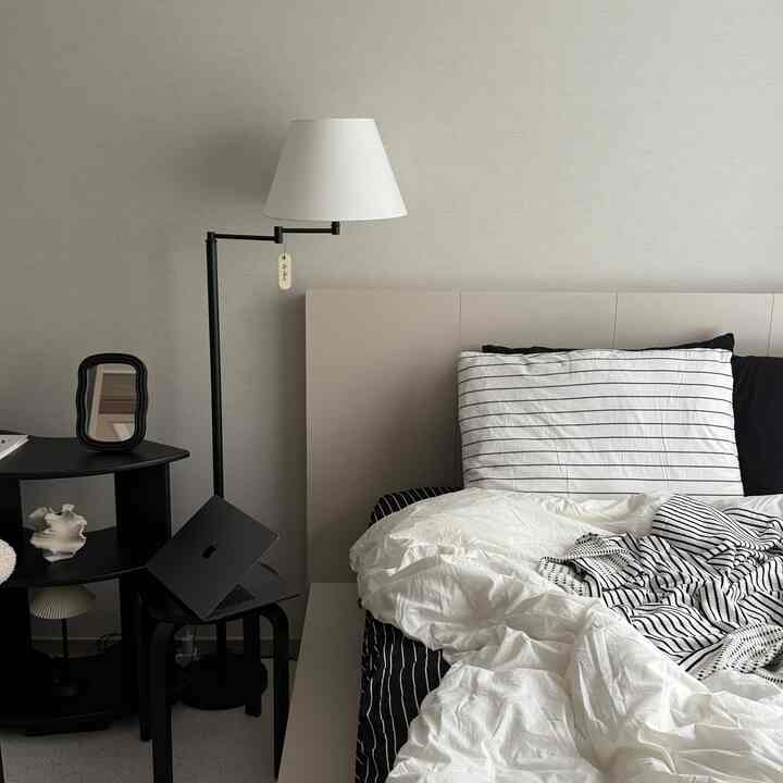 白と黒のトーンのモダンな寝室、ベッドとフロアランプ、小さなサイドテーブルとノートパソコンが配置された空間