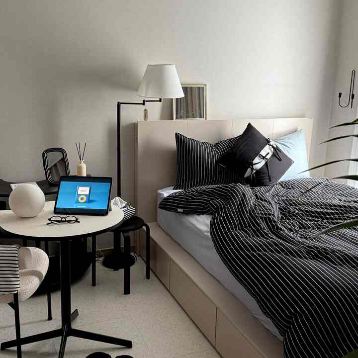 ベージュと黒を基調とした寝室、ミッドセンチュリーモダンの家具が配置され、リモートワーク用のタブレットがある居心地の良いワンルーム