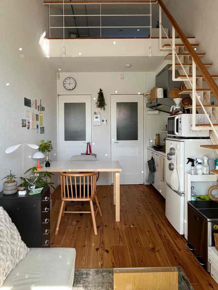 White-walled studio space with natural wood furniture featuring dining area and loft, showcasing a minimal and warm atmosphere