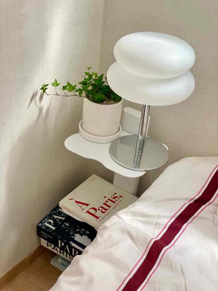 A simple bedroom corner with white and red striped bedding, featuring a white table lamp and small plant on a nightstand