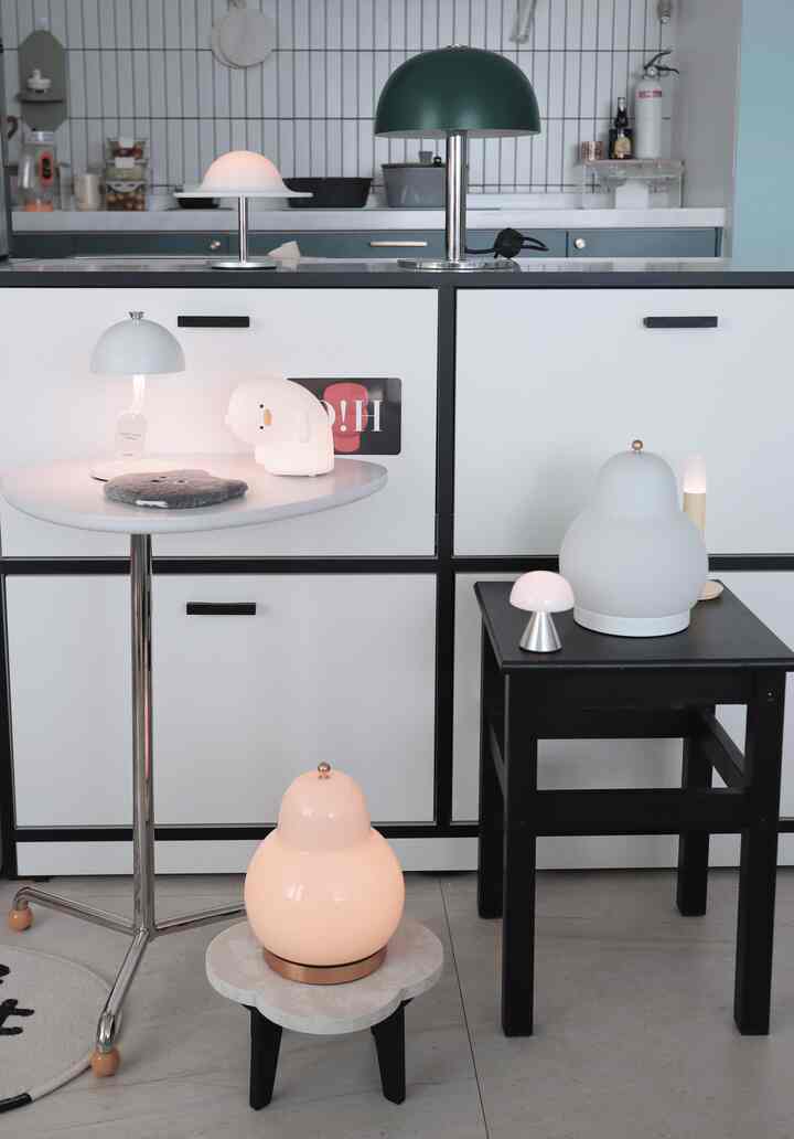 白と黒のトーンのキッチンスペース、サイドテーブルや床に様々なワイヤレス照明が配置された清潔でモダンな雰囲気のインテリア