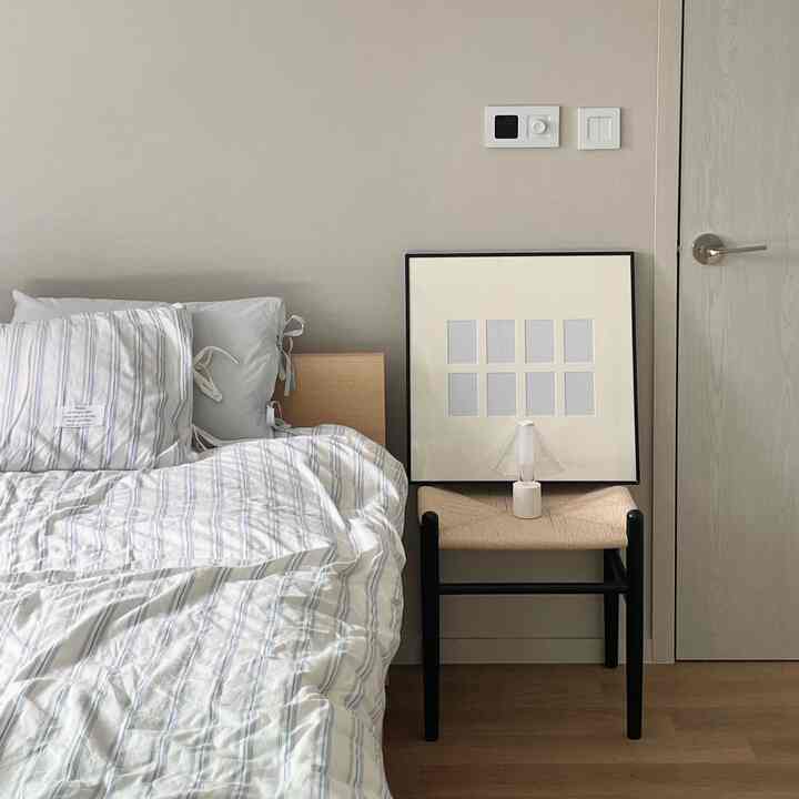 Natural toned bedroom featuring white and wood-tone bedding with a black stool and picture frame, creating a clean aesthetic
