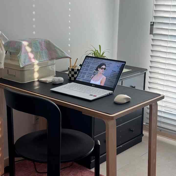 白と黒のトーンのワンルームホームオフィス、黒いデスクと椅子、ノートパソコン、ブラインドが調和した印象的な空間