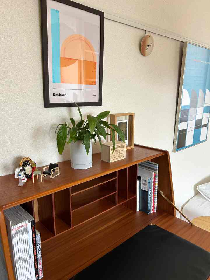 ナチュラルカラーのヴィンテージライティングビューローとバウハウスポスターが配置された落ち着いた書斎空間