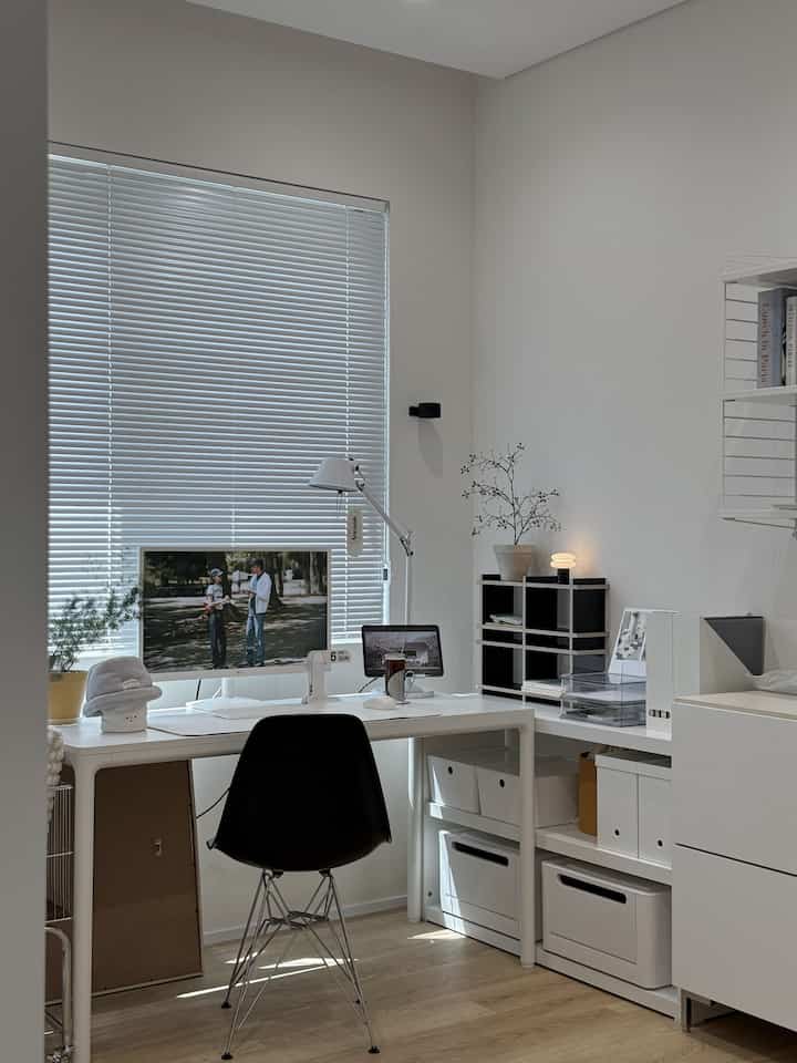 ホワイトとウッドトーンが調和する窓辺のホームオフィス、すっきりと整理されたデスクとコンピュータモニターが配置されたモダンな雰囲気のインテリア
