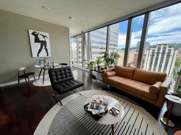 Mid-century modern living room featuring large floor-to-ceiling windows, a leather sofa, and a black armchair creating a bright, open atmosphere