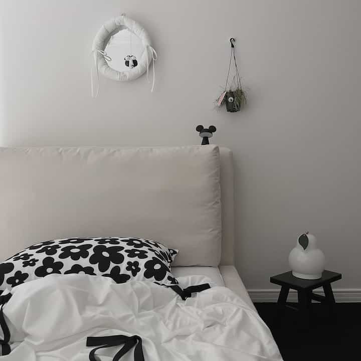 White and black monotone kids' room featuring a bed, stool, round mirror, and plant with a cozy modern atmosphere