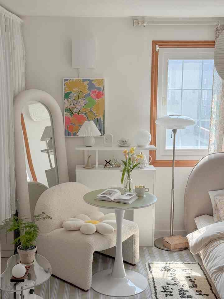 Bright white and beige bedroom-living room featuring a round table, armchair, and floor lamp with a cozy atmosphere