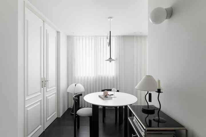 A white and black toned dining room featuring a round dining table and black chairs in a simple, clean layout
