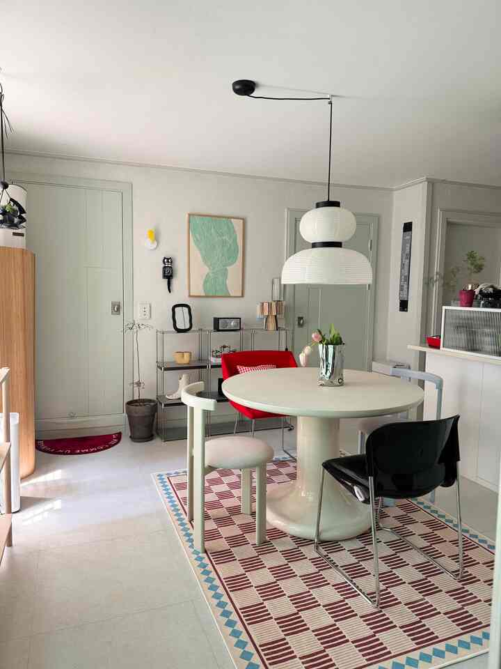 白と赤のトーンのモダンでナチュラルなダイニングルーム、丸テーブルと異なる椅子、ペンダントライトが配置された空間