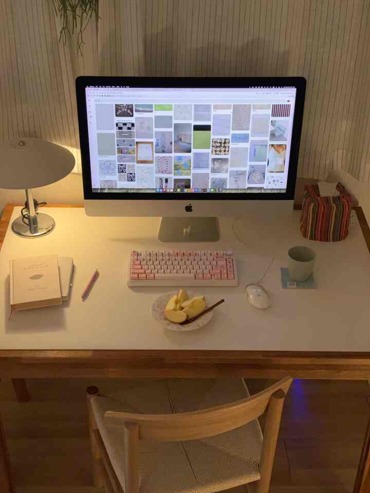 白のランチョンマットが敷かれた木製デスクにコンピューターと照明が配置されたモダンな一人暮らしのホームオフィス