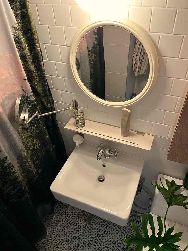 White tiled bathroom with a round mirror above a sink and natural green plant adding freshness to the space